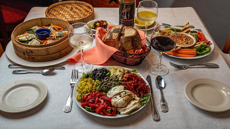 Multiple appetizers with a basket of bread accompanied with white and red wine